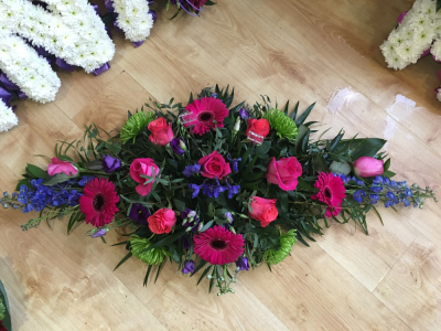 Doube Ended Spray Pink - Double ended spray full of red and pink roses and gerberas and a mix of greenery with blue delphiniums. Flowers may vary according to availability. Includes local delivery.